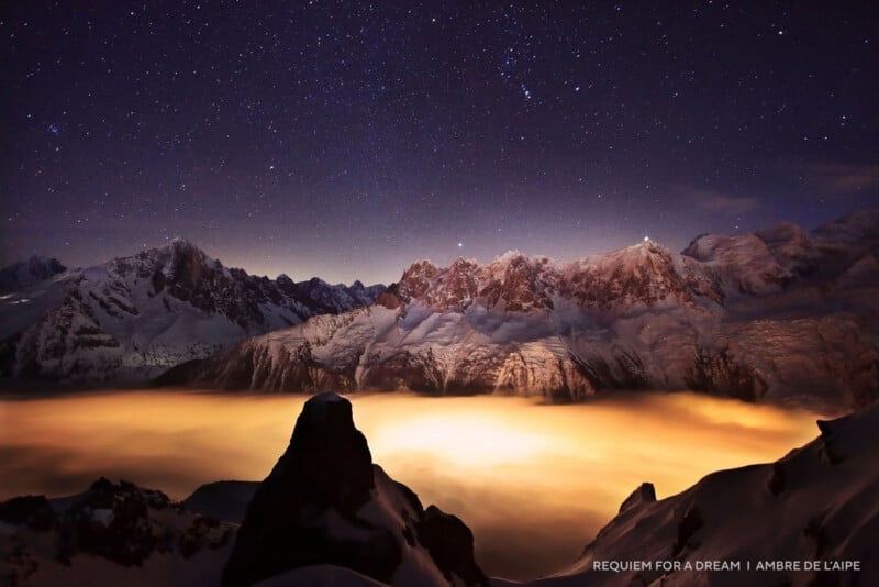 Snowy mountain peaks rise above a glowing sea of clouds under a starry night sky, with a prominent dark rock silhouette in the foreground. Text in the corner reads "REQUIEM FOR A DREAM | AMBRE DE L’AIPE.