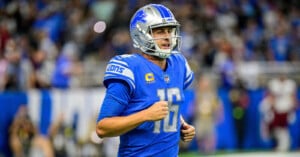 A Detroit Lions football player wearing a blue uniform and helmet with the number 16 on his jersey runs on the field during a game. The crowd is blurred in the background.