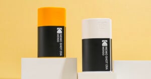 Two rectangular containers, one yellow and one white, with black labels reading “MEMO SHOT ERA MS100,” are displayed on white blocks against a yellow background.