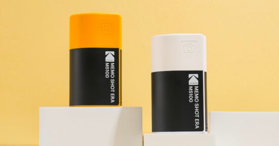 Two rectangular containers, one yellow and one white, with black labels reading “MEMO SHOT ERA MS100,” are displayed on white blocks against a yellow background.