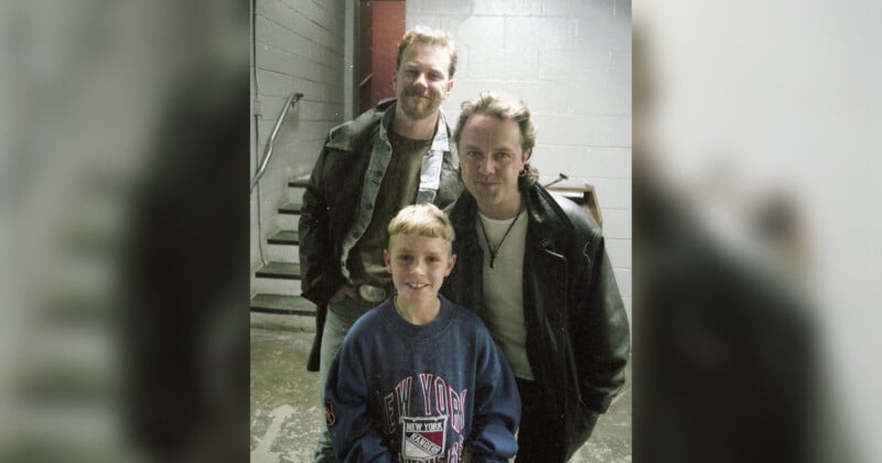 Three people pose together indoors near a staircase. Two adults in leather jackets stand behind a smiling young boy wearing a blue New York sweatshirt. The background features concrete walls and metal stairs.