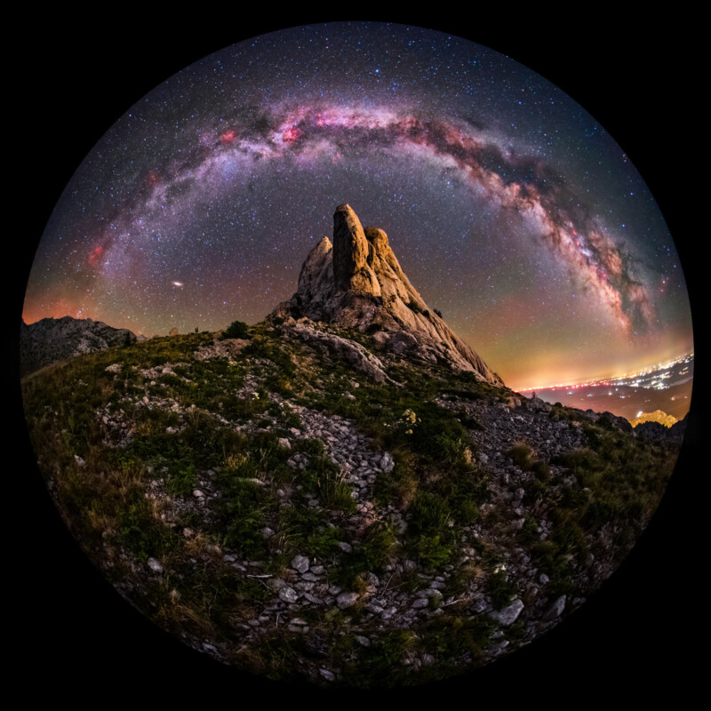 La noche está llena de vibrantes vistas de peces rocosos en la Vía Láctea Arqueada, el cielo y las luces de la ciudad visibles en el horizonte distante están llenas de cielo y luces de la ciudad.