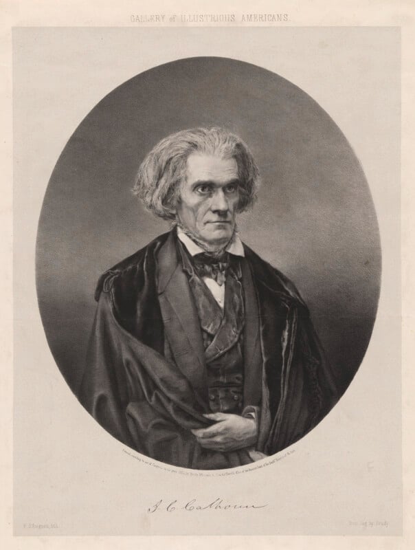 A black and white portrait of an older man with wavy gray hair, wearing a suit with a bow tie and a draped cloak, looking slightly to the viewer’s left. The image has a formal, historical appearance.