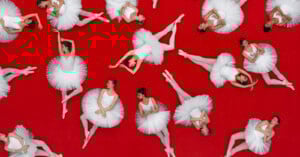Ballet dancers in white tutus and pointe shoes pose gracefully on a vibrant red background, arranged in various elegant positions viewed from above.