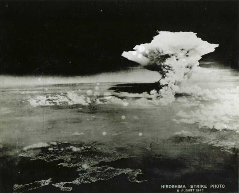 Black-and-white aerial photo showing a large mushroom cloud rising over Hiroshima, Japan, after the atomic bombing on August 6, 1945. Text at the bottom reads “HIROSHIMA STRIKE PHOTO 6 AUGUST 1945.”.