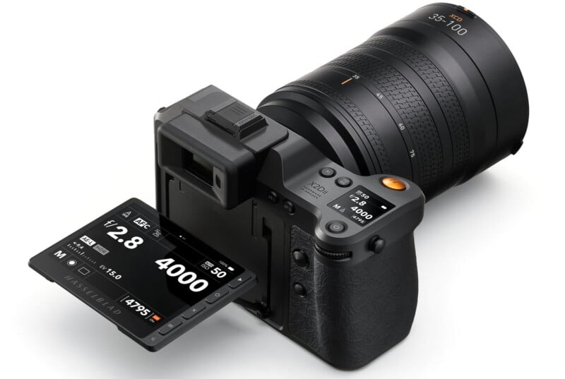 A digital camera with a large lens and a tilting touchscreen display shows camera settings like aperture, shutter speed, ISO, mode, and battery level. The display is flipped out, revealing detailed information to the user.