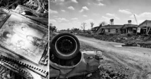 A black-and-white photo shows an old, overturned car on a rough, deserted road lined with damaged houses. On the left, a faded family portrait lies in debris, symbolizing loss amid destruction.