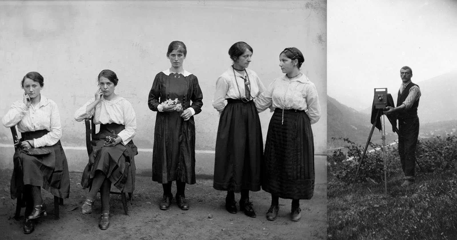 Five young women in early 20th-century dresses pose against a plain wall; two are seated, three stand. To the right, a man stands outdoors with a large vintage camera on a tripod, facing the group.