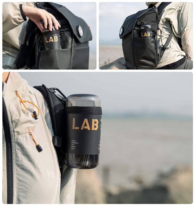 A black backpack with a side pocket holding a cylindrical black bottle labeled "LAB"; the bottle is shown both inside the pocket and attached to the backpack strap, outdoors near water.