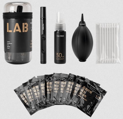 A camera cleaning kit including a brush, cleaning pen, spray bottle, air blower, cotton swabs, container, and several individually packaged wipes, all arranged neatly on a light background.