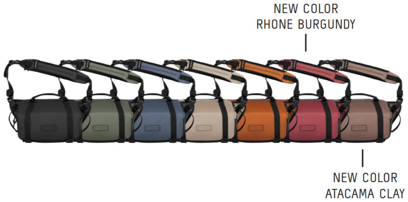 A row of nine camera bags in different colors, including two new colors: Rhone Burgundy (dark red) and Atacama Clay (light brown), labeled with text to indicate the new colors.