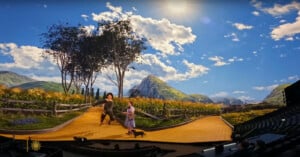 Two people in costume walk along a curved yellow brick road on a stage with a scenic digital backdrop of mountains, trees, and a bright sunny sky, evoking a scene from "The Wizard of Oz.
