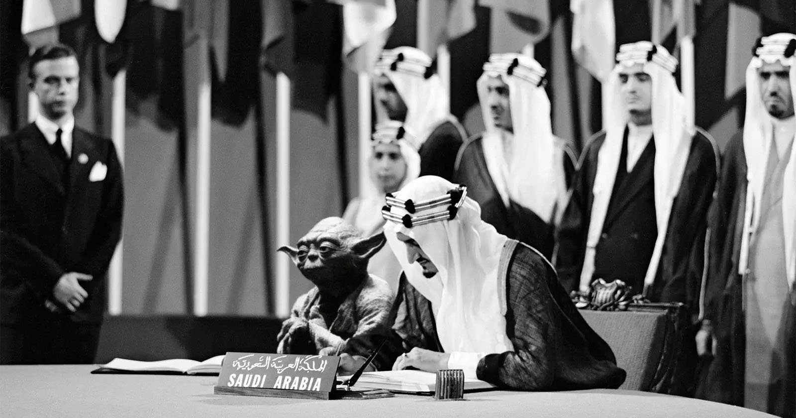 A black-and-white photo shows a person in traditional Saudi Arabian attire signing a document at a conference table labeled "Saudi Arabia," with the Star Wars character Yoda seated beside him. Several men and international flags are in the background.