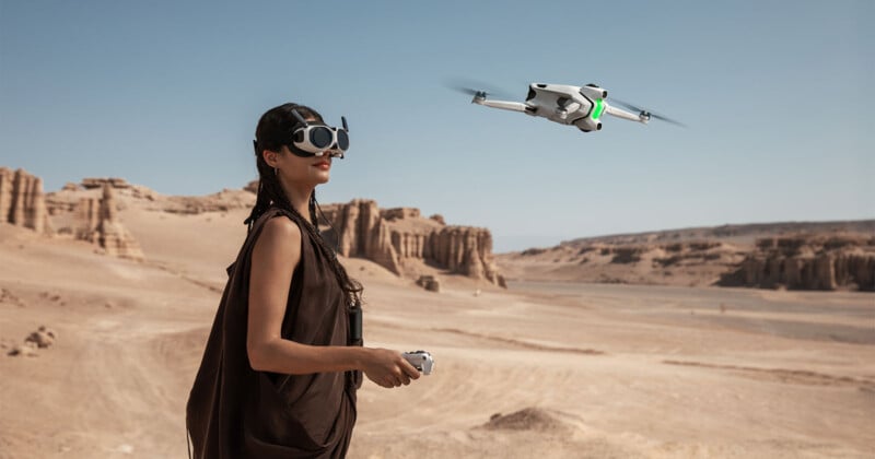 A woman wearing VR goggles operates a drone with a remote control in a vast, rocky desert landscape under a clear blue sky.