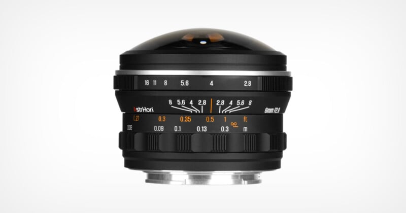 Lente de cámara de gran angular con elemento delantero en forma de domo, enfoque y anillos de apertura muestran marcas de apagado y distancia, que se muestran en un fondo blanco.