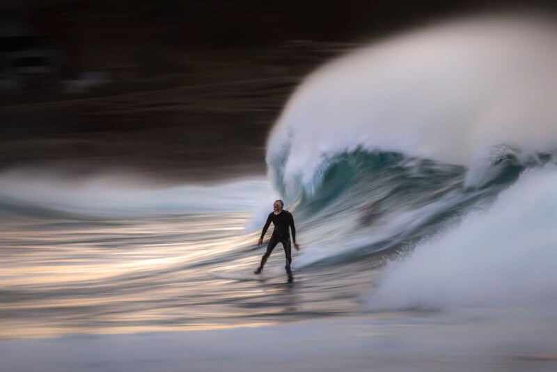 A surfer in a wetsuit rides a large, curling wave at sunset, with water spraying dramatically around them and a blurred background creating a sense of motion and energy.