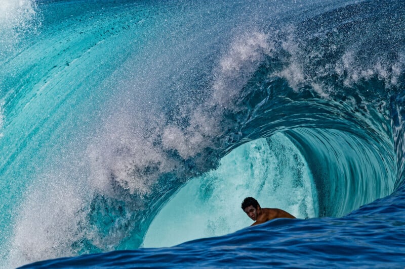 A surfer rides inside the barrel of a powerful turquoise wave, surrounded by churning water and sea spray.
