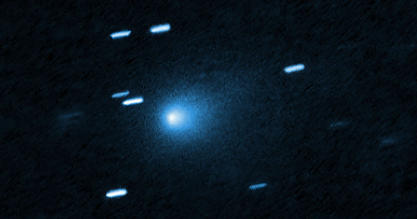 A bright blue comet with a glowing center is surrounded by streaks of light against a dark background, representing stars appearing as trails due to the motion of the comet.