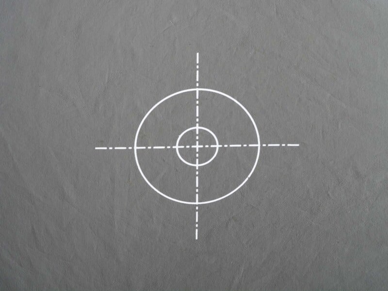 A gray surface with a white target symbol consisting of two concentric circles and four dashed lines intersecting at the center.
