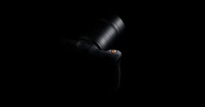 A camera is partially visible in low lighting against a black background, with only the lens and part of the top section highlighted.