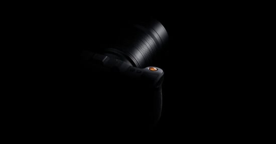 A camera is partially visible in low lighting against a black background, with only the lens and part of the top section highlighted.