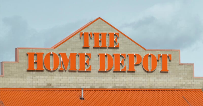 The Home Depot store exterior with large orange letters spelling "The Home Depot" on a beige brick wall and an orange roof below, set against a cloudy sky.