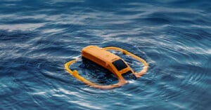 A yellow underwater drone floats on the surface of blue ocean water, surrounded by a yellow ring-shaped flotation device. The device appears to be in operation or testing mode.