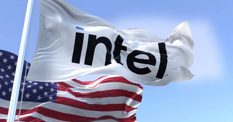 A white flag with the black Intel logo waves in the wind next to an American flag against a blue sky with clouds.