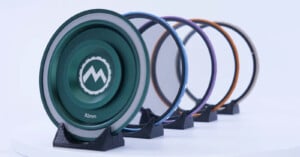 Five colorful camera lens filters, each mounted on individual black stands, are displayed in a line on a white surface. The front filter is green and shows the text "82mm" and a stylized mountain logo.