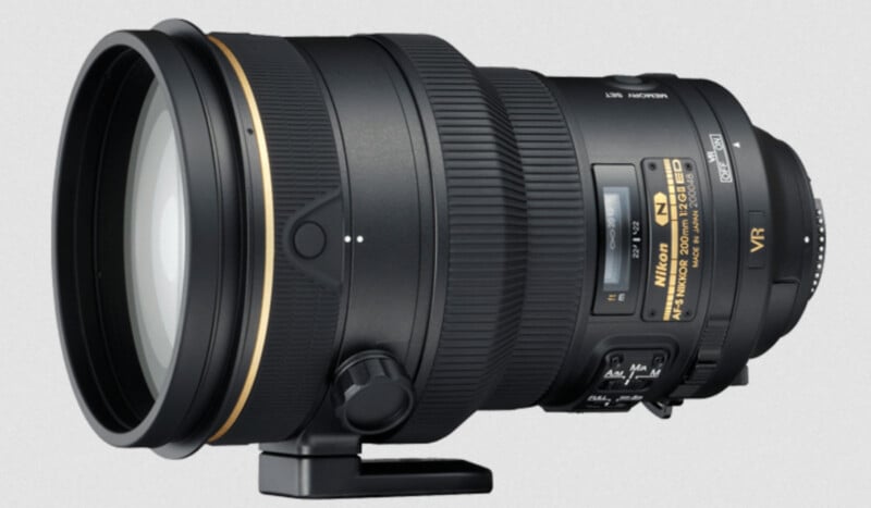 A large Nikon camera lens with a gold ring, tripod mount, and several control switches, displayed against a plain light background. The lens has prominent branding and model information on its side.