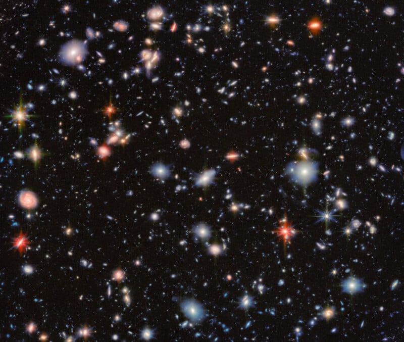 A colorful, star-filled view of deep space showing countless galaxies and stars scattered against a black background, captured by the Hubble Space Telescope. Some stars appear with a glowing halo effect.