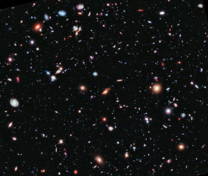 A deep space image showing countless colorful galaxies, stars, and cosmic objects scattered across a black background, captured by the Hubble Space Telescope.