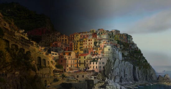 A coastal village with colorful buildings on a rocky cliff is shown in both daylight and nighttime by a diagonal split, highlighting the contrast between bright and dark lighting on the landscape and structures.