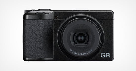 A black compact digital camera with a textured grip, large circular lens labeled "GR LENS f=18.3mm 1:2.8", and the letters "GR" in silver on the bottom right corner of the front.