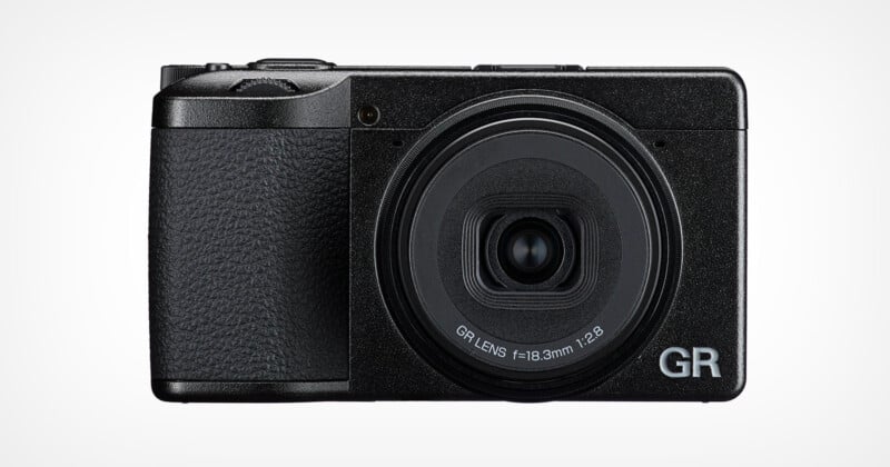 A black compact digital camera with a textured grip, large circular lens labeled "GR LENS f=18.3mm 1:2.8", and the letters "GR" in silver on the bottom right corner of the front.