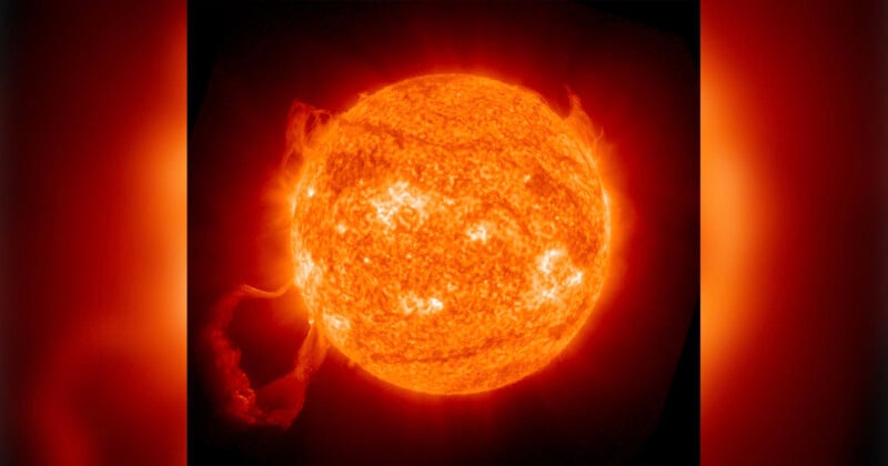 A bright, glowing orange sun with visible fiery solar flares and prominences extending outward against a dark background.