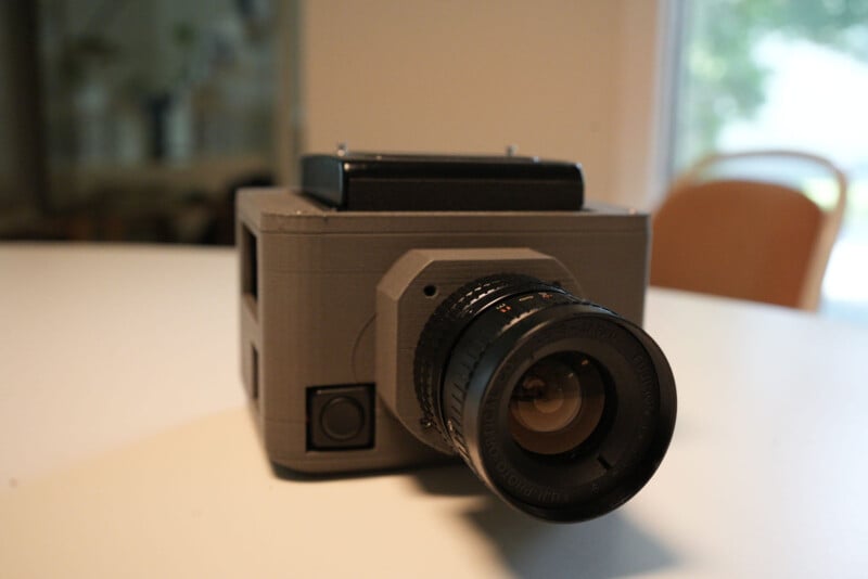 A close-up of a vintage-style camera with a large lens, placed on a white surface with a blurred indoor background.