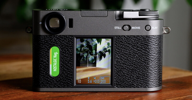 A close-up of the back of a digital camera with a textured black grip, displaying a screen showing a photo of leafy plants and camera settings, and a green button labeled "NOSTALGIC Neg." on the left side.