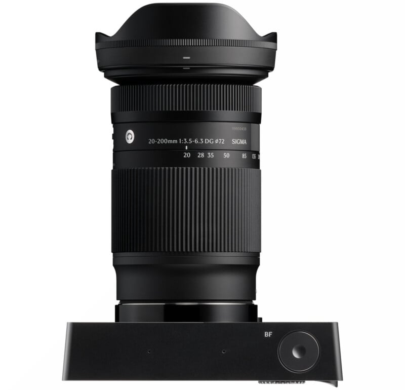 A black Sigma 20-200mm f/3.5-6.3 DG DN lens is standing vertically on a Sigma USB dock, with clear markings for focal lengths and settings on the lens barrel.