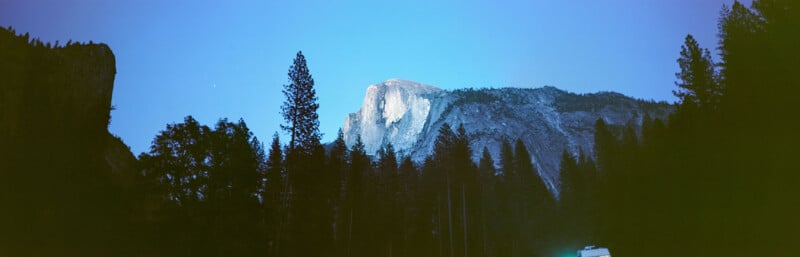 Vista de Yosemite de Half Dome Mountain al anochecer, con pinos más altos en primer plano y cielo azul claro y profundo sobre la cabeza.