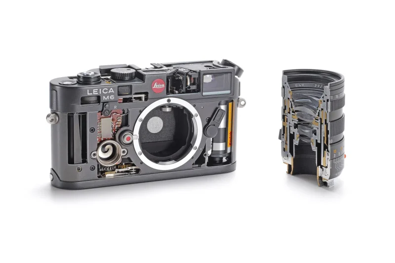 A Leica M6 camera and lens are shown cut in half, revealing their detailed internal components and mechanics. The camera is on the left, and the cross-section of the lens is on the right, both against a white background.
