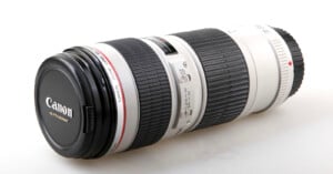A Canon Ultrasonic telephoto camera lens with a black lens cap, white body, black rubber grip, control switches, and red accent ring, placed on a white surface.