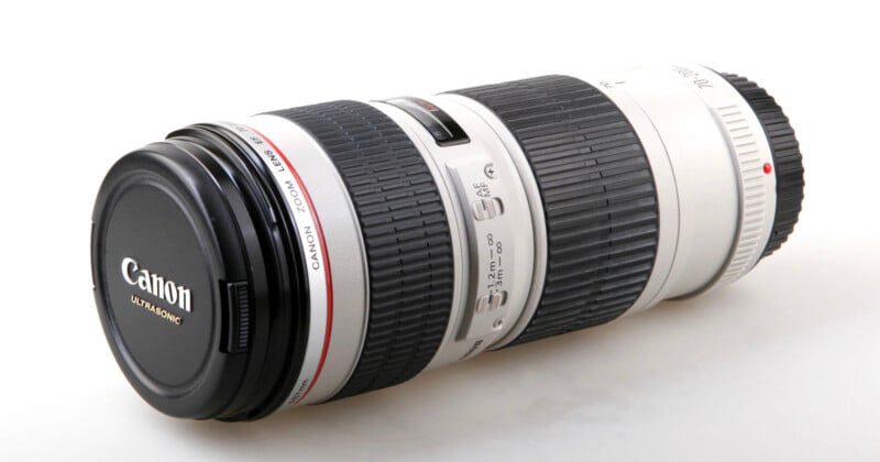 A Canon Ultrasonic telephoto camera lens with a black lens cap, white body, black rubber grip, control switches, and red accent ring, placed on a white surface.