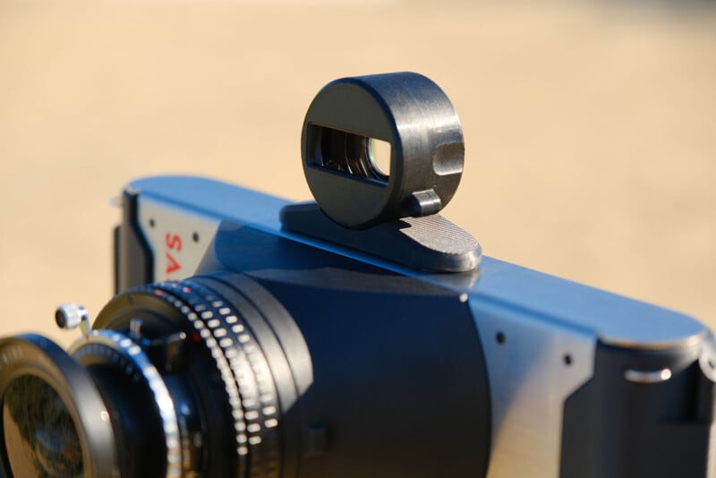 Un primer plano de la cámara con un accesorio de visor rectangular impreso en 3D está montado en la parte superior con la lente y parte del cuerpo de la cámara enfocado en un fondo borrosa.