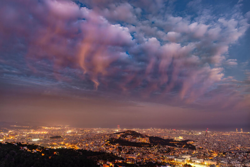 En la vista panorámica de la ciudad al anochecer, hay luces de la ciudad brillantes debajo, exudando nubes coloridas dramáticas en el cielo, creando una atmósfera vibrante y vibrante.