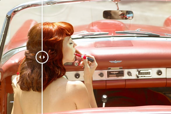 A woman with red hair applies lipstick while sitting in the driver’s seat of a vintage red convertible. A split effect shows different tones on each half of the image. The dashboard and rearview mirror are visible.