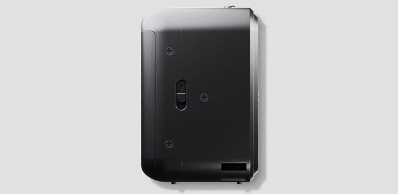 A black rectangular electronic device viewed from the side, featuring screws, a small switch labeled "7," and a vent opening on a plain light gray background.