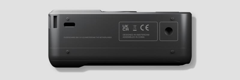 Close-up view of the bottom of a black electronic device showing regulatory labels, certification marks, and the text "DESIGNED IN AMSTERDAM, ASSEMBLED IN CHINA" on a light gray background.