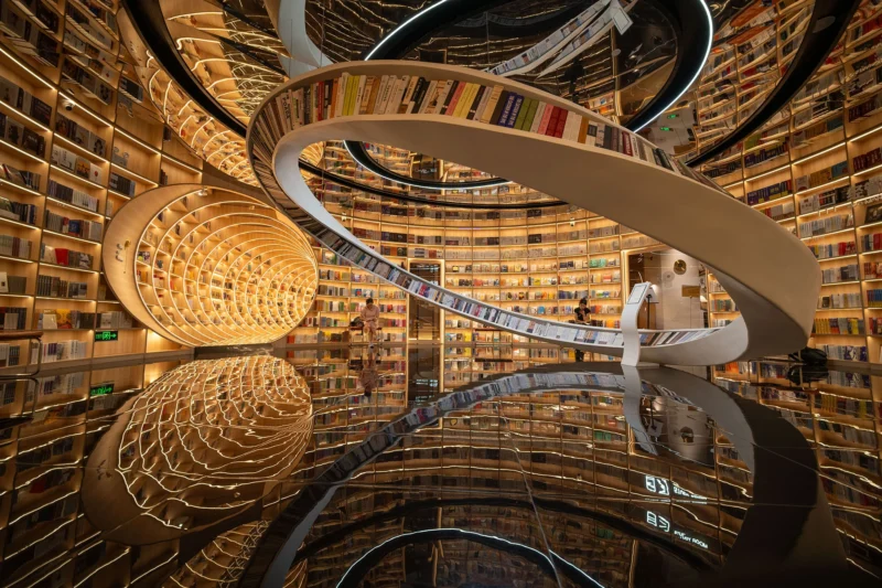 Una biblioteca futurista con estantería curva, escalera de caracol, iluminación cálida y pisos espejados forman la fantasía de espacios infinitos llenos de libros y detalles arquitectónicos brillantes.