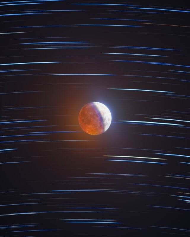 A reddish moon appears in the center of a dark sky with blue and white star trails streaking horizontally in the background, suggesting long exposure photography.